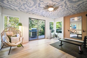 Una habitación con ventilador de techo, una silla de mimbre, una cinta de correr y un espejo grande.