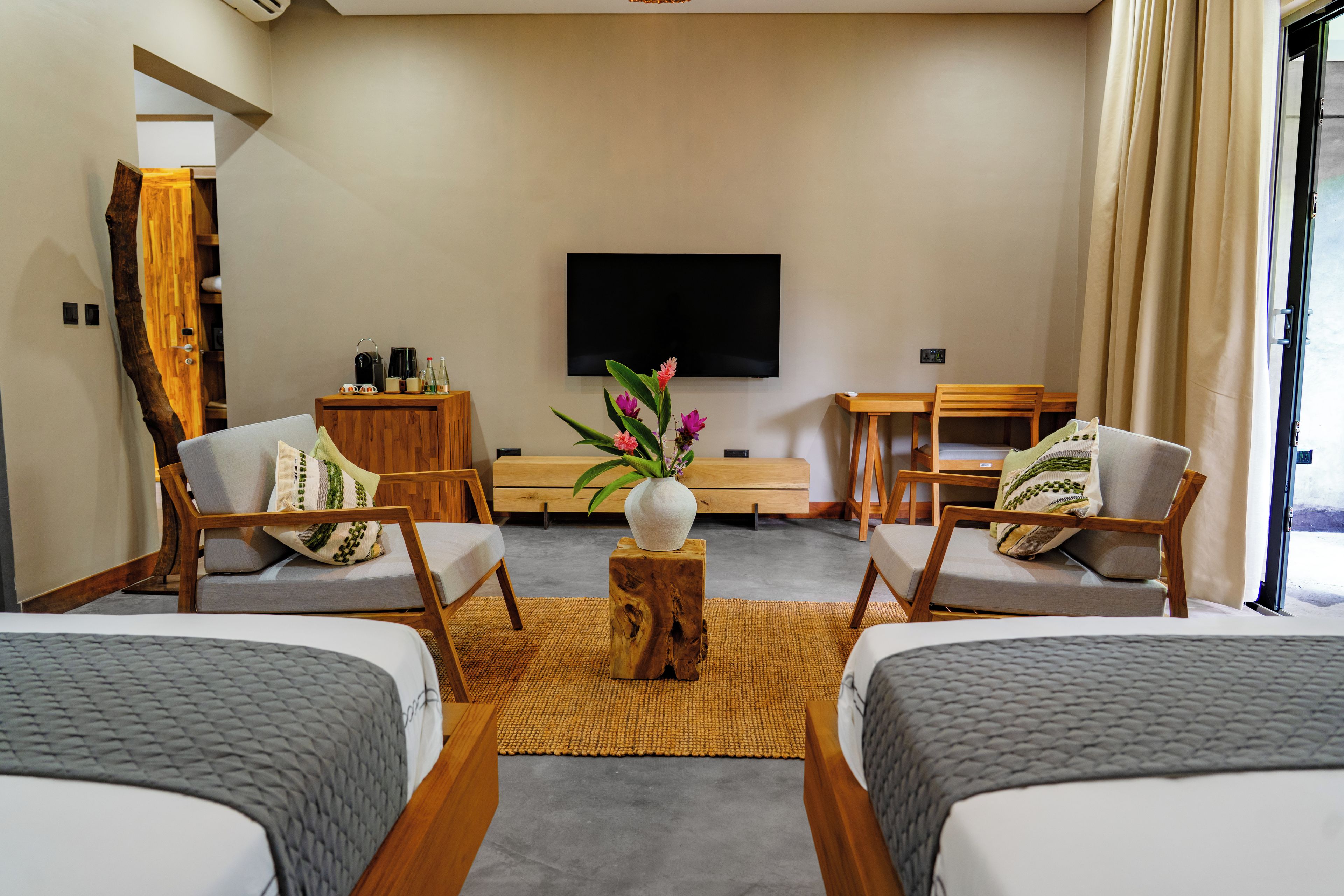 A modern hotel room with two beds, a flat-screen TV, a wooden coffee table, and a large window with curtains.