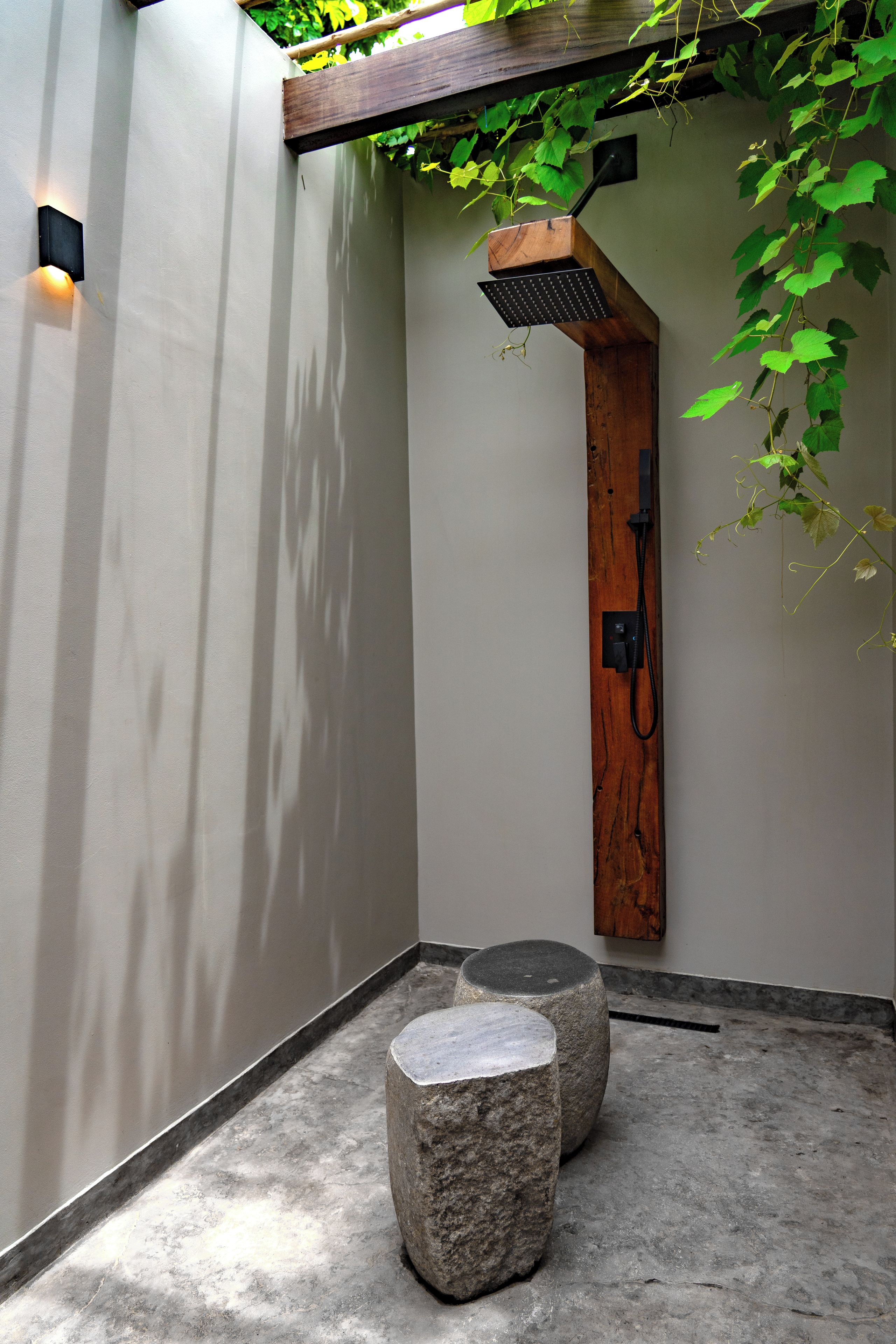 A modern shower area with a wooden structure, a stone bench, and a concrete floor.