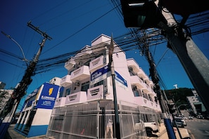 Un edifici de diversos pisos amb balcons, un cartell que diu 'Avenida do Estado' i un cartell blau que diu 'ILUMISUL'.