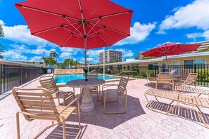 A poolside area with lounge chairs, a table, and red umbrellas. - Coastal Studio Retreat, Updated Kitchen/Bath, Private Beach, Casa Mar Resort (Sarasota)