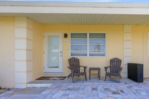 A building with a yellow exterior, a door with a number 2, two Adirondack chairs, a small table, and a black object that could be a speaker or a TV. - Coastal Studio Retreat, Updated Kitchen/Bath, Private Beach, Casa Mar Resort (Sarasota)