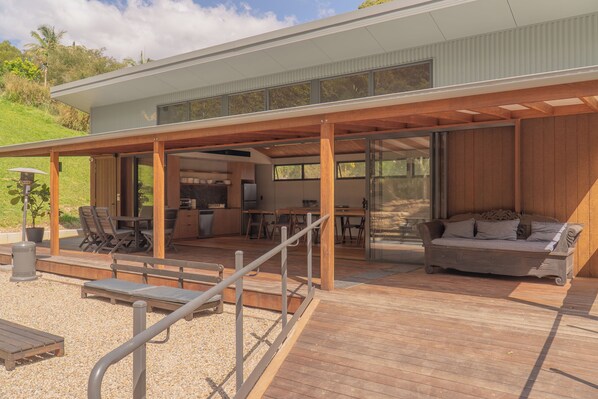 A modern house with a covered patio area, outdoor seating, and a kitchen visible through large windows.