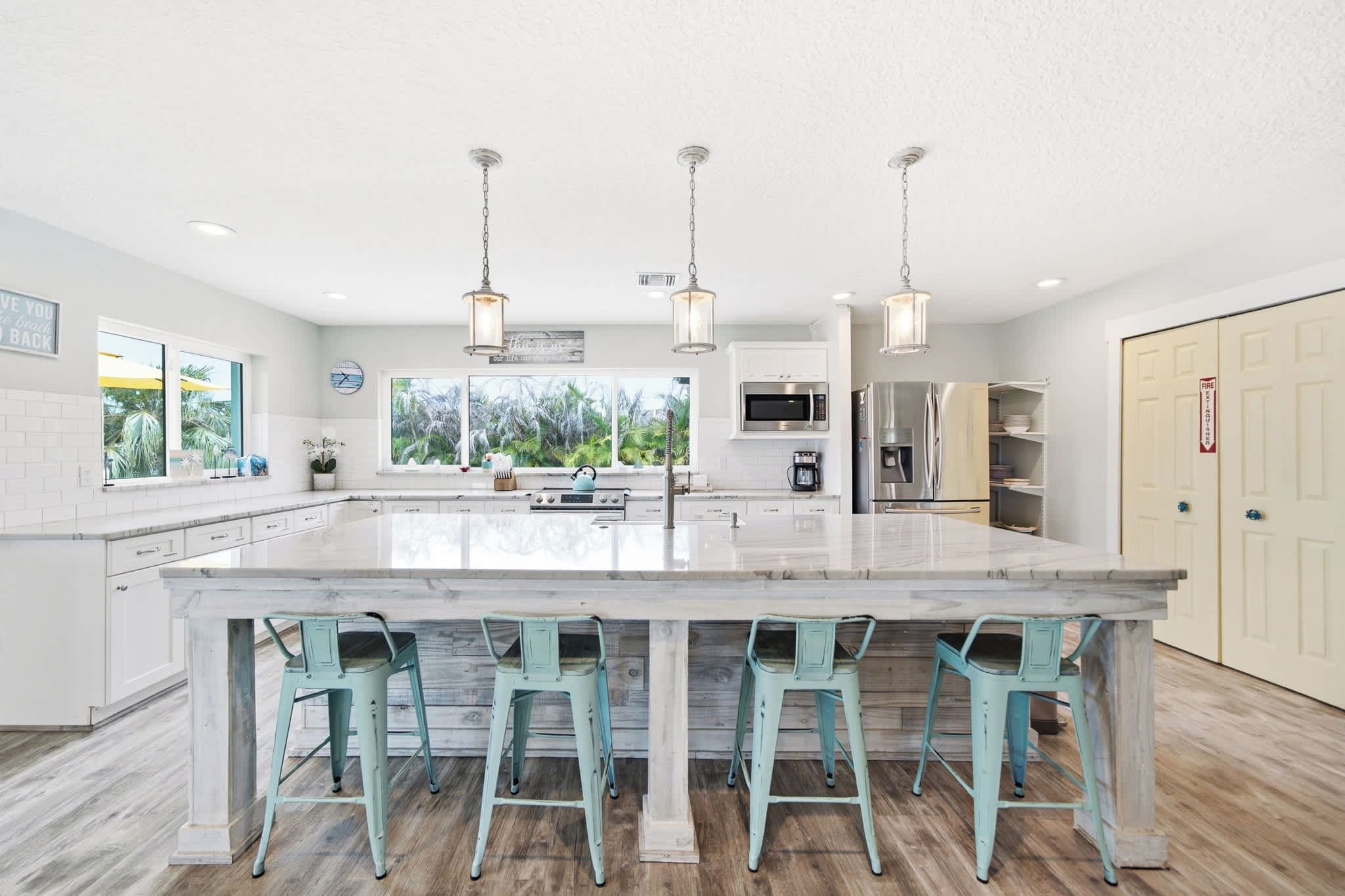 A modern kitchen with a large island, bar stools, stainless steel appliances, and a view of the outdoors.