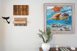 A wall with a wooden sign reading 'HOME,' a wall-mounted coat rack, a framed painting of a sea turtle, and a potted plant. - Canalfront 4BR with Pool, Dock & Kayaks (Cocoa Beach)