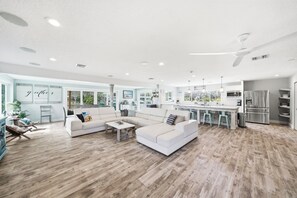 A spacious living area with a large sofa, a coffee table, and a kitchen with modern appliances. - Canalfront 4BR with Pool, Dock & Kayaks (Cocoa Beach)