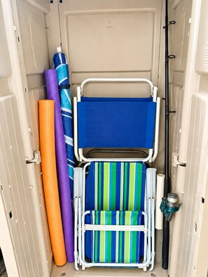 A storage unit with a blue folding chair, a striped cushion, and rolled-up mats. - 2BR/2.5BA Gated Beachside Townhome (Cape Canaveral)