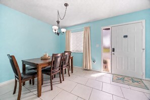 A dining area with a table and chairs, a chandelier, a window with curtains, and a door with a star-patterned mat. - 2BR/2.5BA Gated Beachside Townhome (Cape Canaveral)