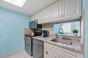 A compact kitchen with a microwave, stove, dishwasher, and a sink. - 2BR/2.5BA Gated Beachside Townhome (Cape Canaveral)