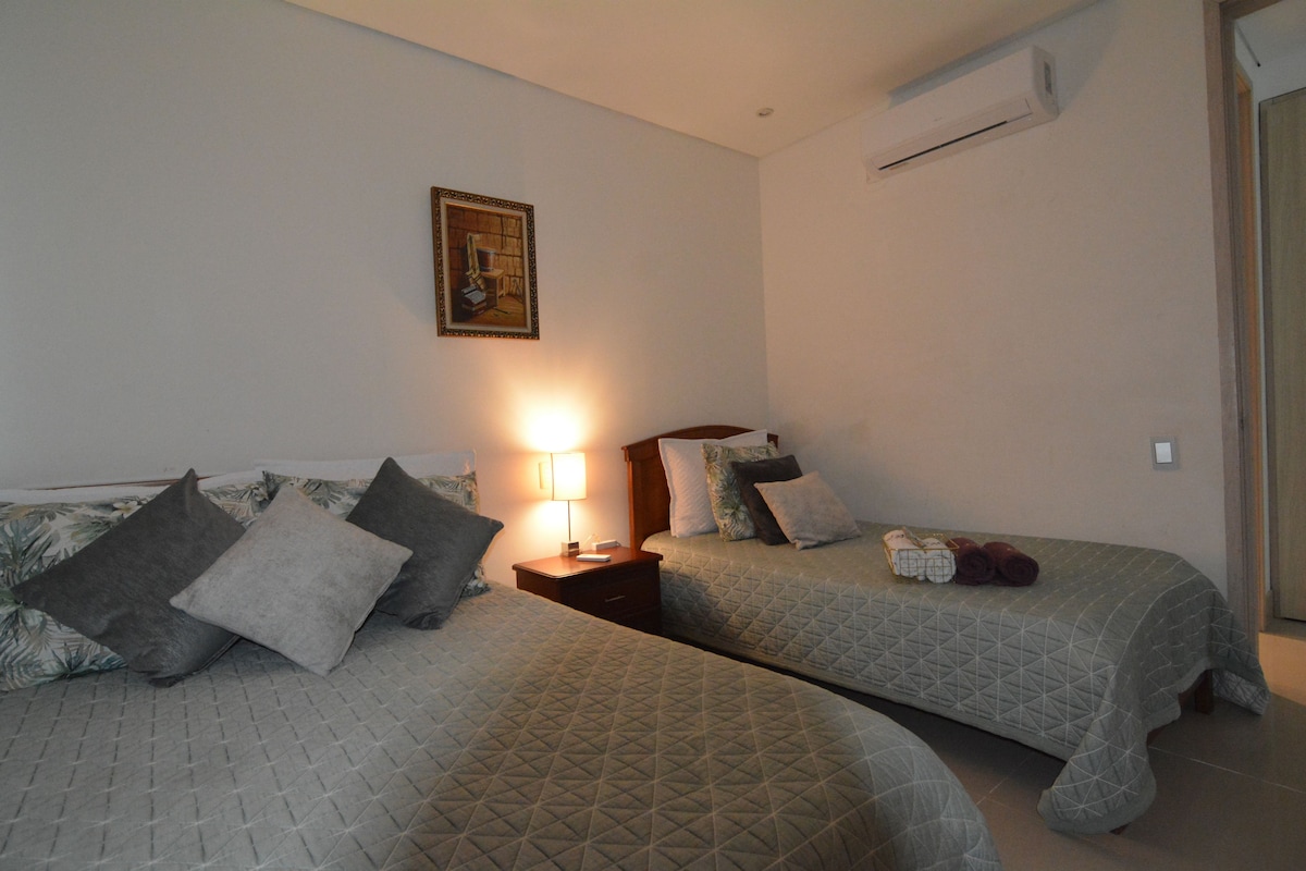 Una camera d'albergo con due letti, un comodino con una lampada e un condizionatore d'aria a parete.