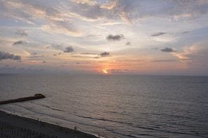 Una spiaggia con un molo che si estende verso il mare, onde che lambiscono dolcemente la riva e un tramonto sullo sfondo.