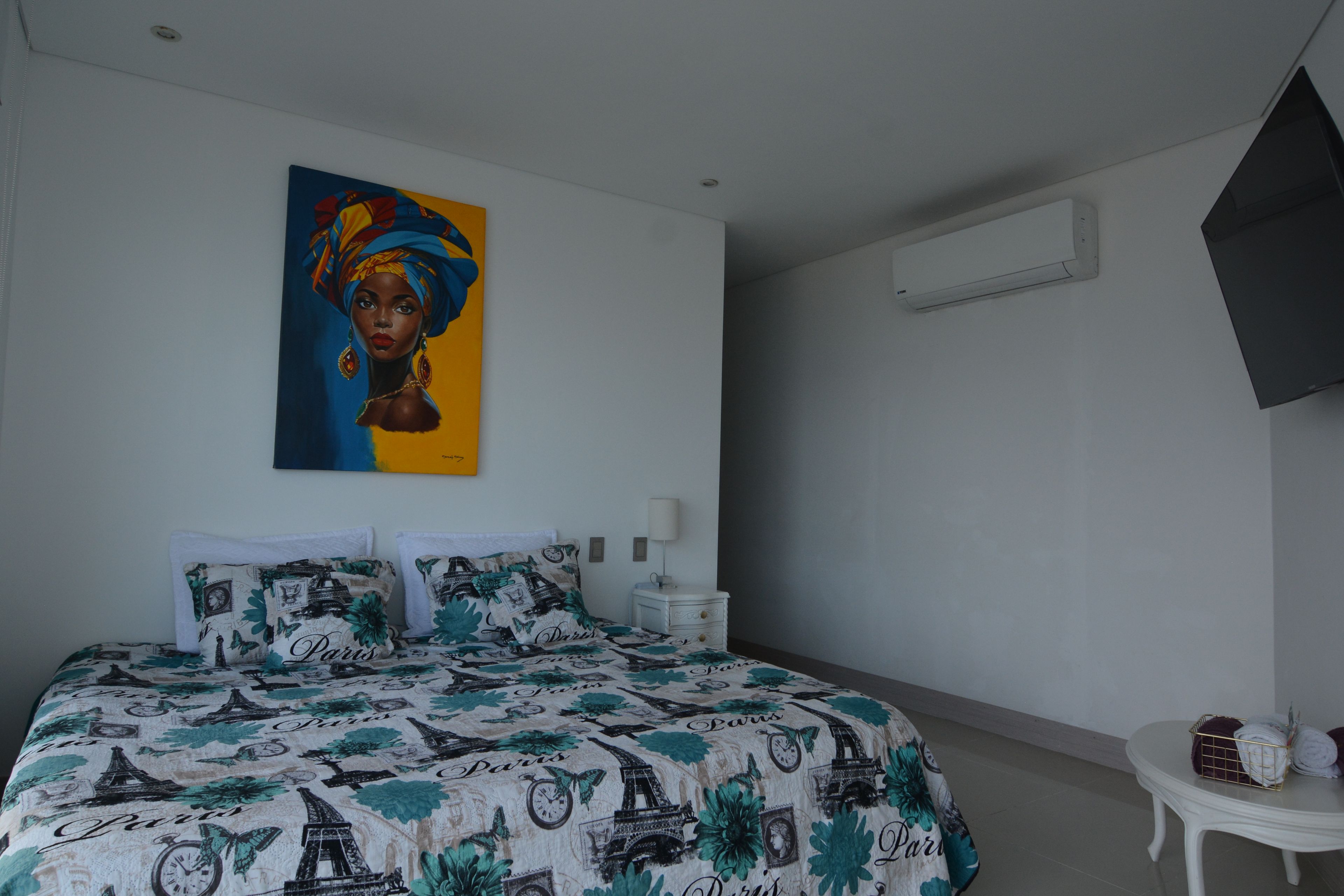 Een slaapkamer met een bed, nachtkastje, een wandairconditioner en een schilderij.