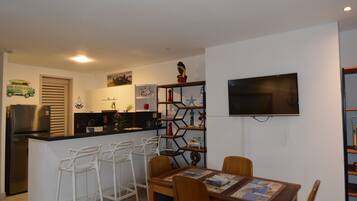 Een moderne keuken met een inbouweiland, barstoelen, een eettafel met stoelen, en een flatscreen televisie aan de muur.
