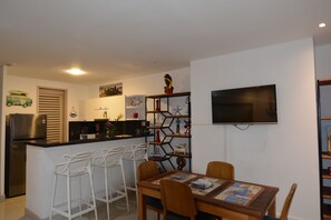 A modern kitchen with a built-in island, bar stools, a dining table with chairs, and a flat-screen TV mounted on the wall. - Oasis Apartment (Cartagena de Indias)