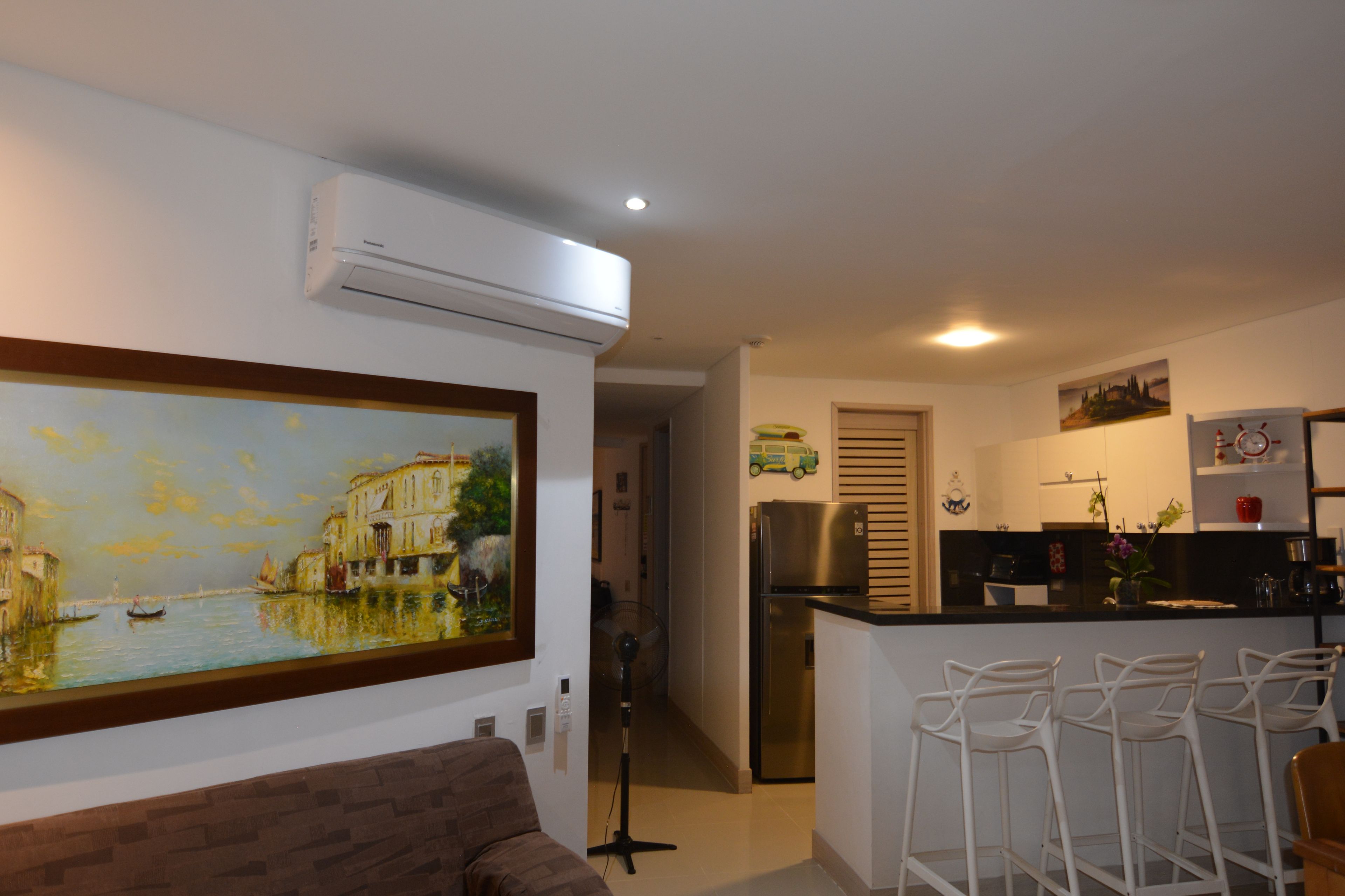 Een moderne keuken met een centraal eiland, witte barkrukken en een schilderij van een gracht.