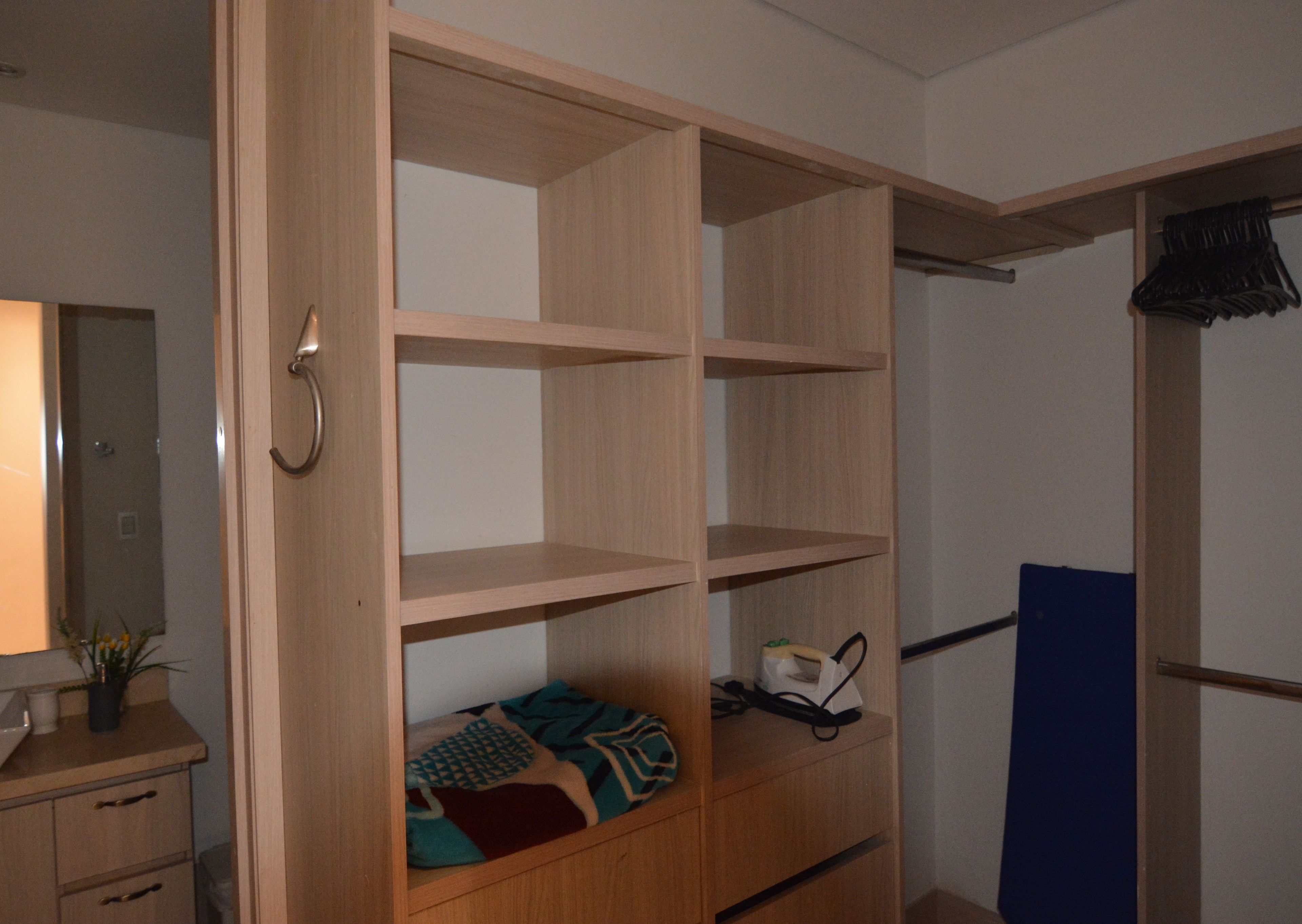 Armadio a muro con ripiani aperti, un letto con coperta fantasia e una parete divisoria blu.
