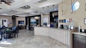 Eine moderne Hotelhalle mit einer gebogenen Rezeption, einer Sitzecke mit Stühlen und Tischen, einem großen Flachbildfernseher und einer Wand mit Stadtbild-Mural.