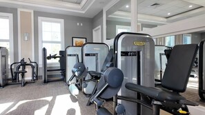 A gym with various exercise machines, including leg extension machines, and large windows allowing natural light. - Spacious 5-bedroom townhome in enchanting Davenport close to Disney (Davenport)