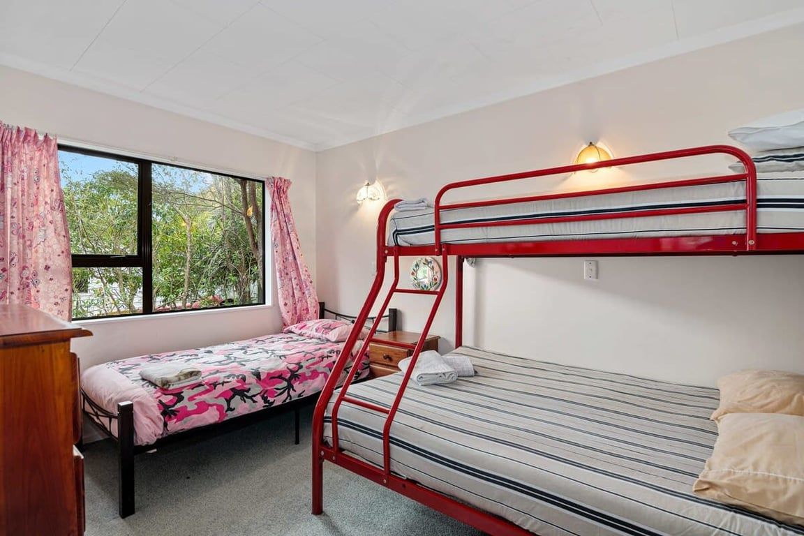 A dormitory room with two bunk beds, a desk, a window with curtains, and a wall-mounted light fixture.