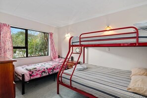 A dormitory room with two bunk beds, a desk, a window with curtains, and a wall-mounted light fixture.