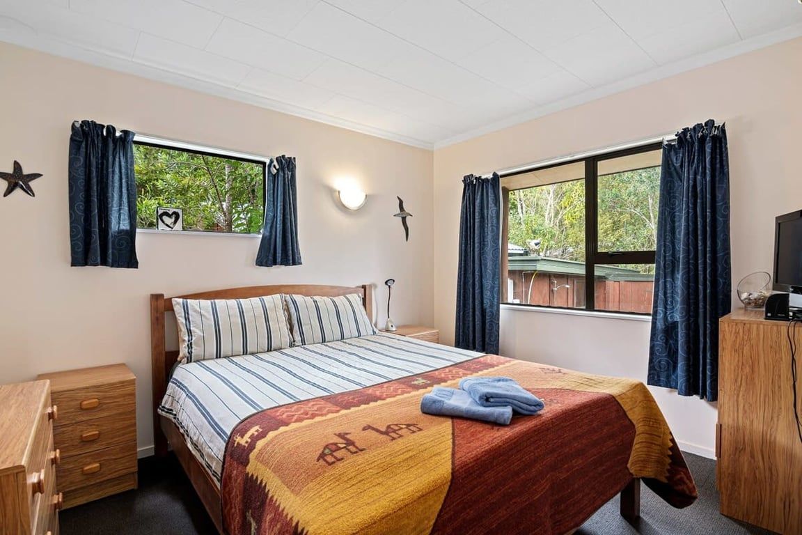 Ein Schlafzimmer mit einem Bett, einem Nachttisch, einer Kommode, einem Fernseher und Vorhängen.