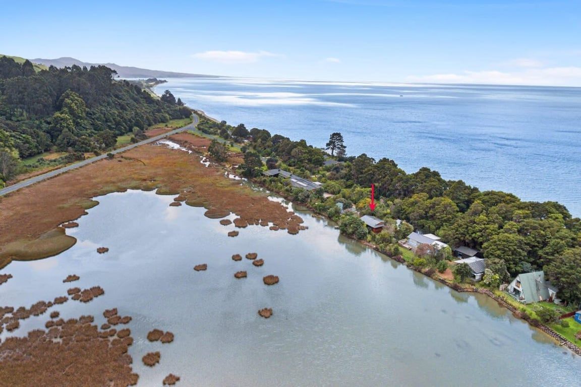 A coastal landscape with a road, a body of water, and a cluster of houses.