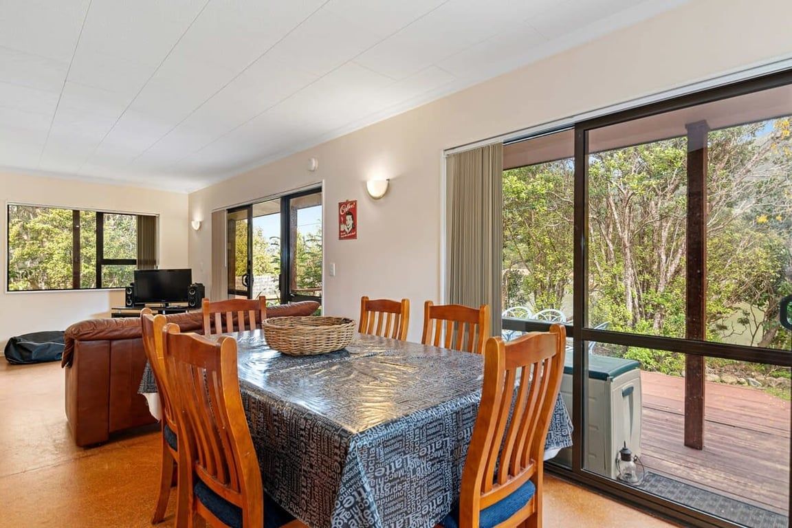 A dining area with a table covered in a patterned tablecloth, surrounded by wooden chairs.