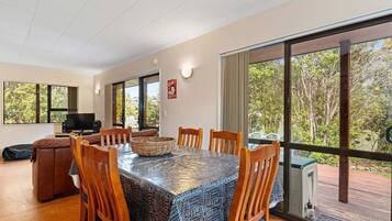 A dining area with a table covered in a patterned tablecloth, surrounded by wooden chairs.