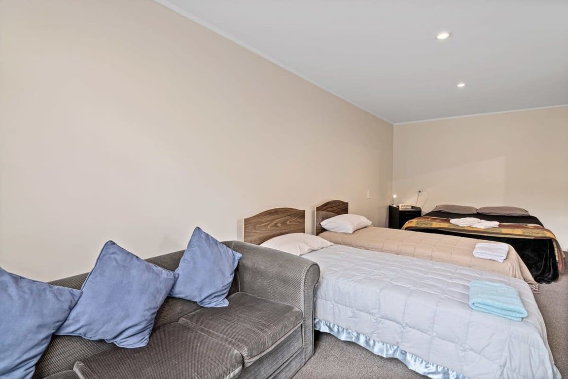 A hotel room with a sofa, two beds, and a nightstand.
