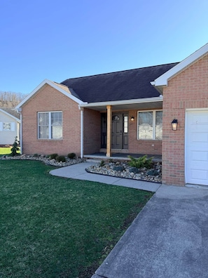 A two-story brick house with a covered front porch, a garage, and a well-maintained lawn.