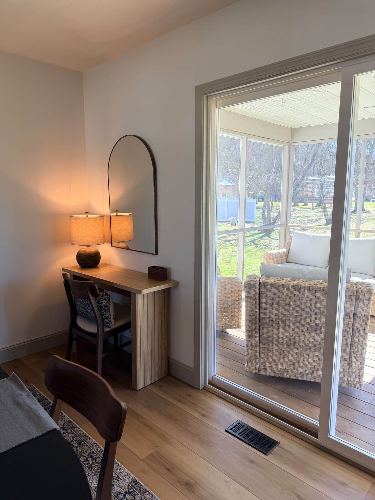 Ett rum med ett skrivbord, en stol, en lampa och en skjutdörr i glas som leder ut till en sittplats utomhus.