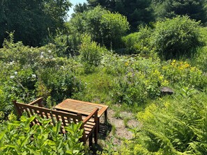 Een houten tafel en stoelen in een tuin met verschillende planten en bloemen.
