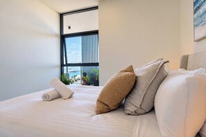 Une chambre d’hôtel avec une grande fenêtre, un lit parfaitement fait et une vue sur le paysage urbain.