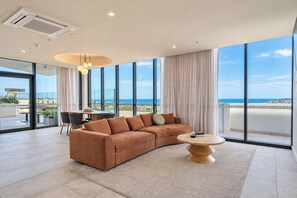Un salon moderne avec un canapé d’angle, une table basse ronde et de grandes fenêtres donnant sur la mer.