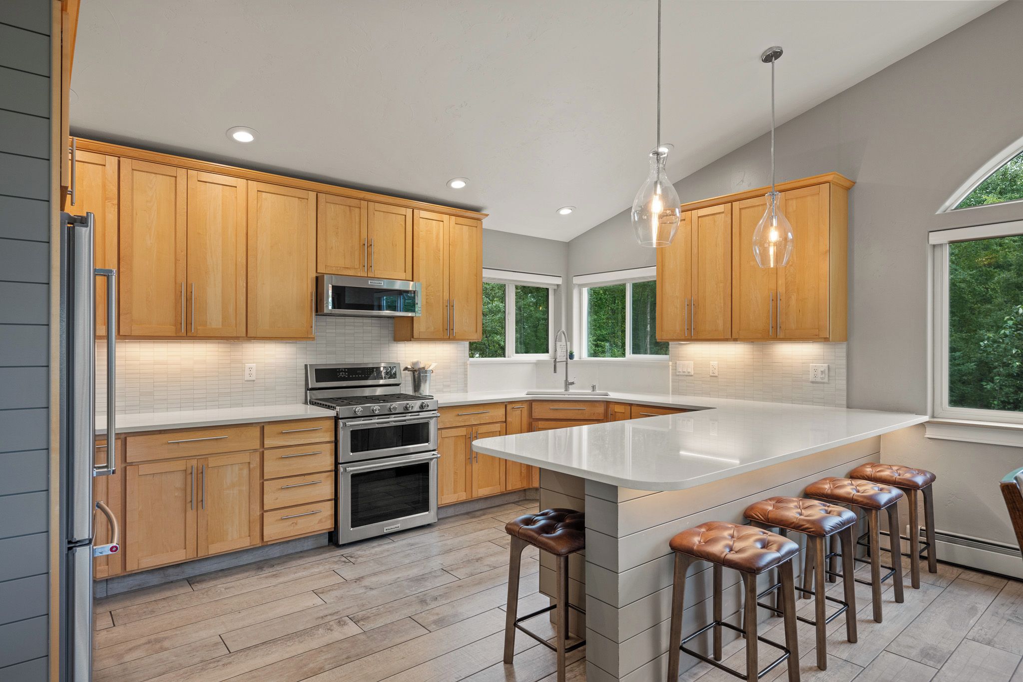 A modern kitchen with wooden cabinets, stainless steel appliances, a large island with bar stools, and pendant lighting.
