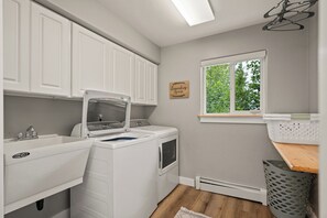 A laundry room with a washing machine, dryer, and a window with a view of trees. - The Chugach Retreat-Spacious Luxury, Views & Hot Tub, Sleeps 10, FlexibleBooking (Anchorage)