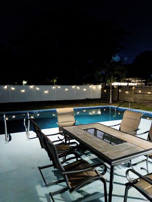 An outdoor pool area with a table and chairs, surrounded by a white fence and string lights. - 3-bedroom house in pleasant Sarasota (Sarasota)