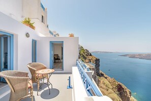 Un balcón con mobiliario de mimbre, vistas al mar y un edificio con detalles azules.