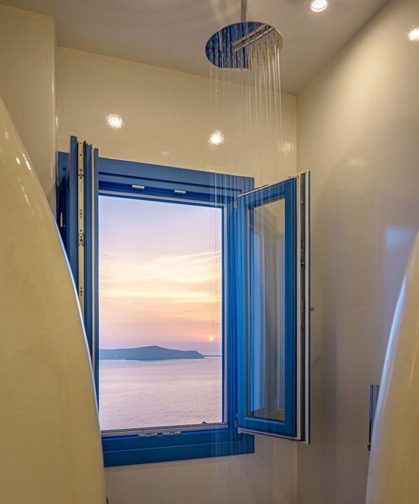 Un baño con un ventanal grande, un cabezal de ducha y vistas al mar.