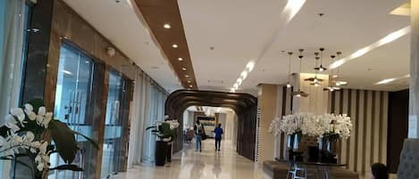 Un vestíbulo de hotel con piso pulido, una recepción y plantas en macetas.