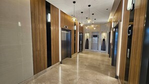 A modern hotel corridor with elevators, wooden paneling, and pendant lighting. - MOA Complex 1BR Shore 3 Tower 1 Unit 547 (Pasay)