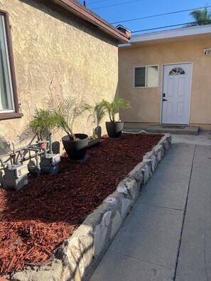 A landscaped area with mulch, potted plants, and outdoor equipment. - Cozy 1-bedroom house in pleasant Los Angeles with AC (Los Angeles)