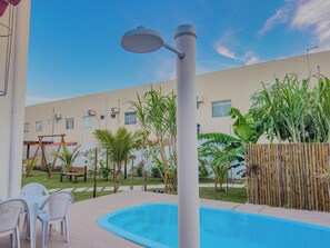 Ein Pool mit Pergola und Liegestühlen, umgeben von Grünpflanzen und einem Gebäude mit Fenstern und Klimaanlagen.