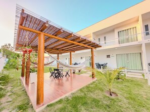 A covered outdoor seating area with a hammock, a table with chairs, and a small garden. - Duplex Apartment 4 with 2 Suites 450m from the Beach in Santa Cruz Cabrália (Santa Cruz Cabrália)