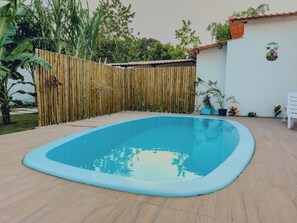 A rectangular swimming pool with a tiled deck, surrounded by a bamboo fence, potted plants, and a white wall with a decorative sign. - Duplex Apartment 4 with 2 Suites 450m from the Beach in Santa Cruz Cabrália (Santa Cruz Cabrália)