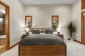 Ein Schlafzimmer mit einem hölzernen Bett, zwei Nachttischen, einer Topfpflanze und Blick ins Freie durch Fenster.