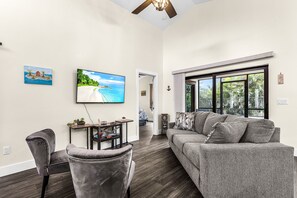Ein Wohnzimmer mit grauem Sofa, einem grauen Sessel, einem Fernseher und einem kleinen Tisch mit einer Pflanze.