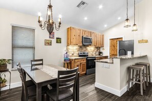 A modern kitchen with wooden cabinets, a central island, and a dining area with a table and chairs. - NEW!! Bokeelia Bonita! Pool 2 bed 2 bath home! (Bokeelia)