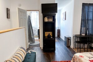 Ein kompakter Wohnbereich mit einer Couch, einem kleinen Tisch, einem Fernseher und einem Schrank mit der Aufschrift 'ROOMS'.