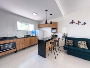 A modern kitchen with a central island, wooden cabinets, and a dining area with a sofa and chairs. - Duplex Apartment 3 with 2 Suites 450m from the Beach in Santa Cruz Cabrália (Santa Cruz Cabrália)